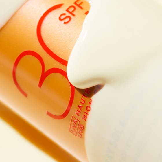 Nuxe Sun Spray SPF30 184 g anti-aging solskydd i en skimrande guldflaska placerad i klart blått vatten