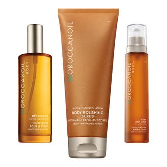 Moroccanoil kroppsvårdset med serum, kroppsolja och kroppsskrubb i bärnstensfärgade flaskor och en skimrande bronstub.