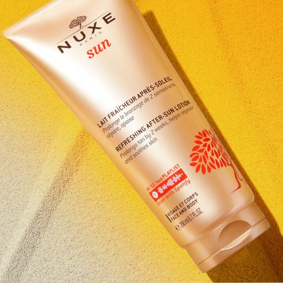 Nuxe Sun Refreshing After Sun Lotion 200 ml i tub på sand som ger 24h hydrating och hjälper till att behålla solbrännan.