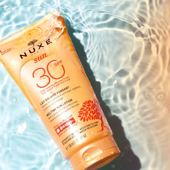 Nuxe Sun Delicious Lotion 150 ml solkräm för ansiktet och kropp i orange tub som flyter i glittrande vatten.