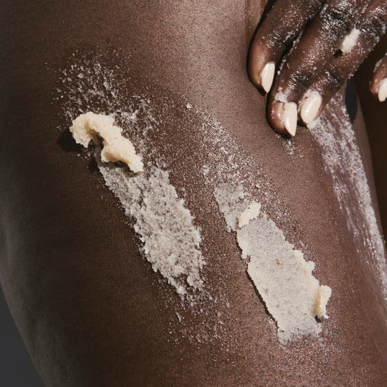 Sol de Janeiro Bum Bum Body Scrub 220 g i gul burk med kornig textur som ger huden lyster på turkost kakel.