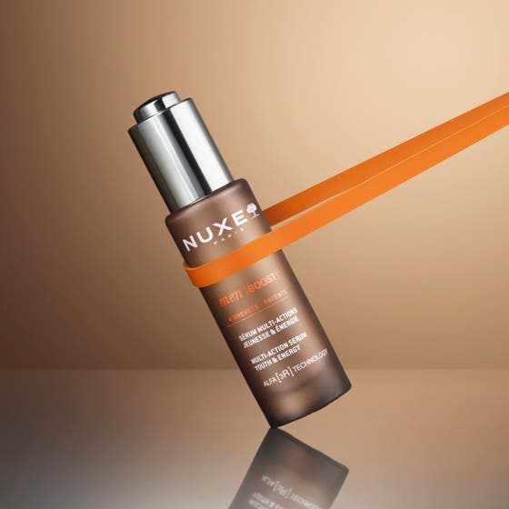 Nuxe Men Multi Action Serum 30 ml ger huden energi på en leende man som rör vid sitt välvårdade ansikte.