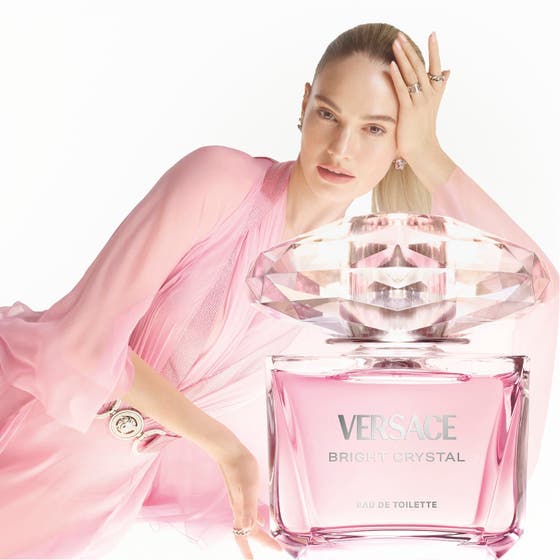 Versace Bright Crystal parfymset blommig parfym i rosa glasflaska bredvid kvinna i rosa klänning