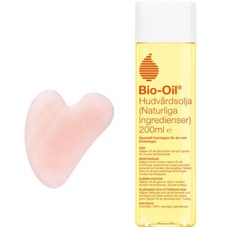 Bio-Oil Hudvårdsolja 200 ml mot ärr och bristningar i plastflaska intill en rosa hjärtformad gua sha sten
