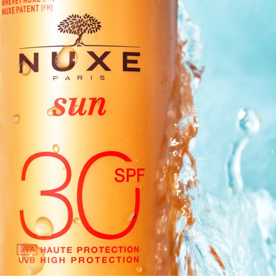 Nuxe Sun Spray SPF30 184 g anti-aging solskydd med krämig vit formula som rinner över den orange flaskan